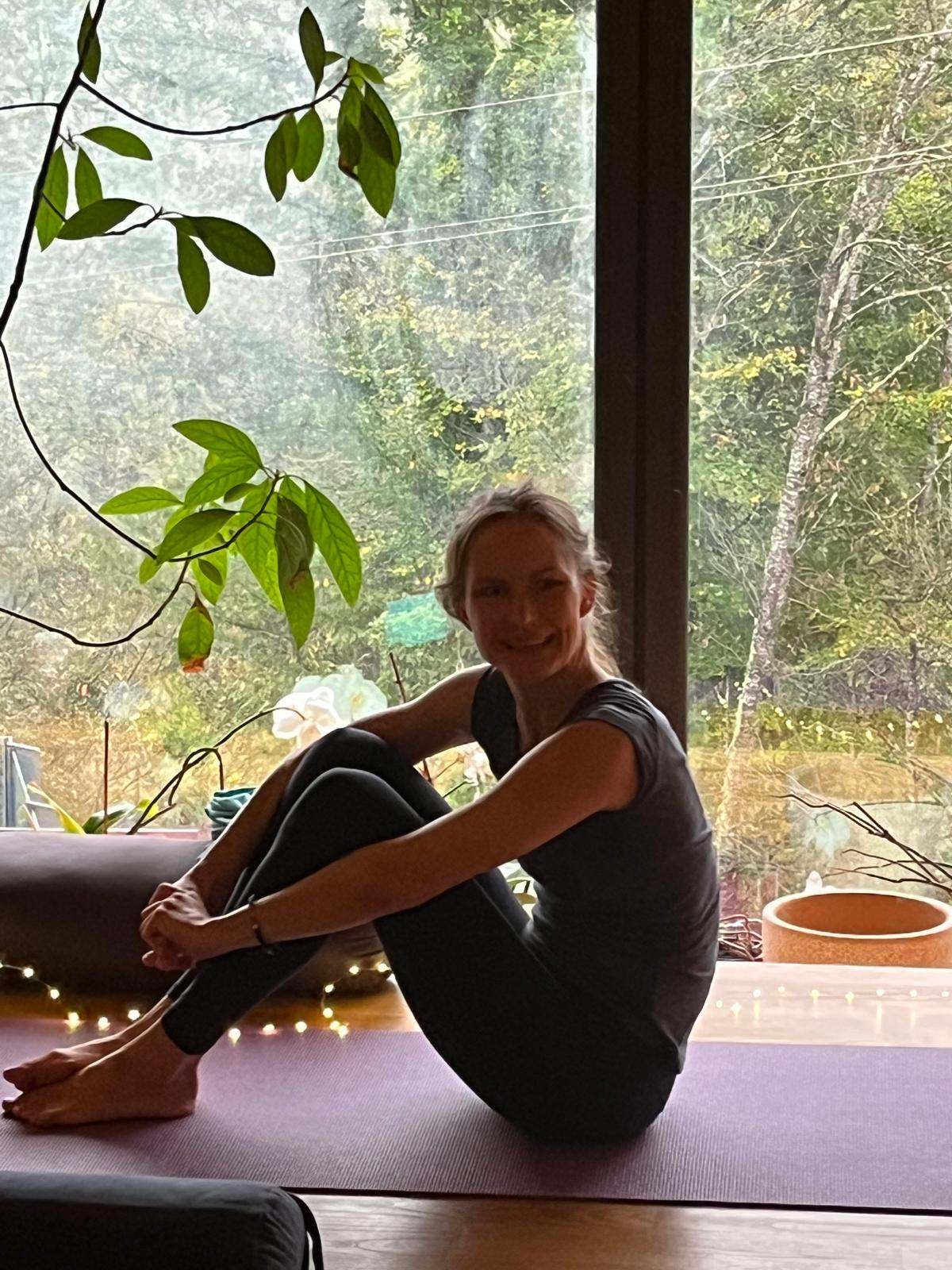 Ulrike Oct2025 Femme pratiquant Real Yoga assise sur un tapis, souriante, jambes croisées.